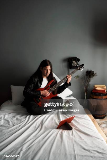 a young boy is learning to play the bass guitar in his room. - bass gitarre stock-fotos und bilder