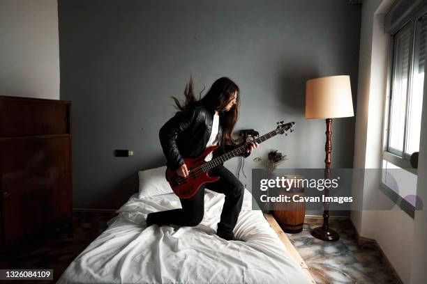 a man with long hair playing bass guitar on the bed - bass player bildbanksfoton och bilder