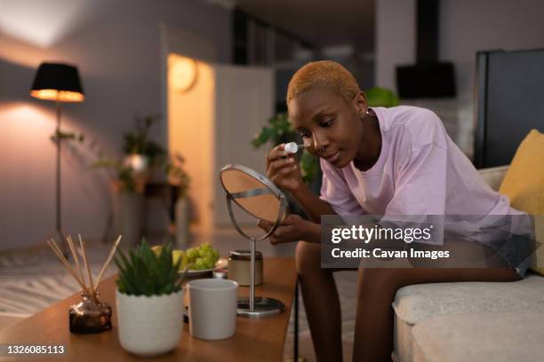 black woman applying cosmetic product on face at home - african american women wet stock-fotos und bilder