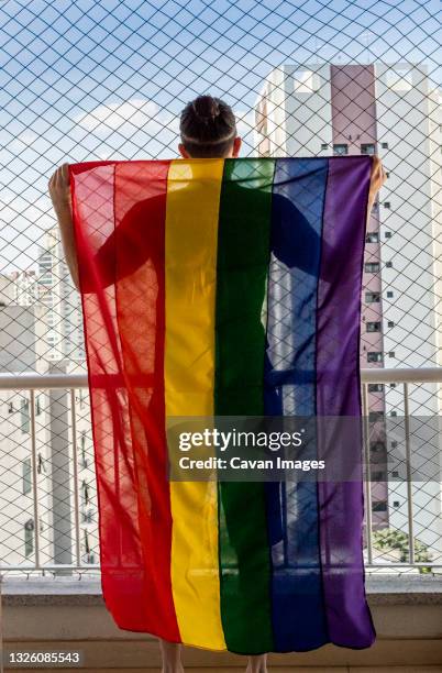 gay man holding the rainbow flag symbol of gay pride on a balcon - generation x icon stock pictures, royalty-free photos & images