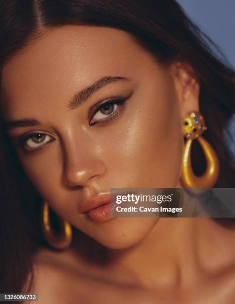 beautiful woman smooth long hair brunette evening make up with liner tanned skin beautiful female portrait over blue background wearing gold earrings - bräune stock-fotos und bilder