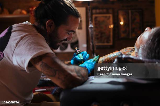 tattoo artist enjoys while working on a customer's arm in his studio. - tattooing stock pictures, royalty-free photos & images