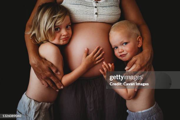 young boys touching mom's pregnant big belly looking at camera - gravida stock-fotos und bilder