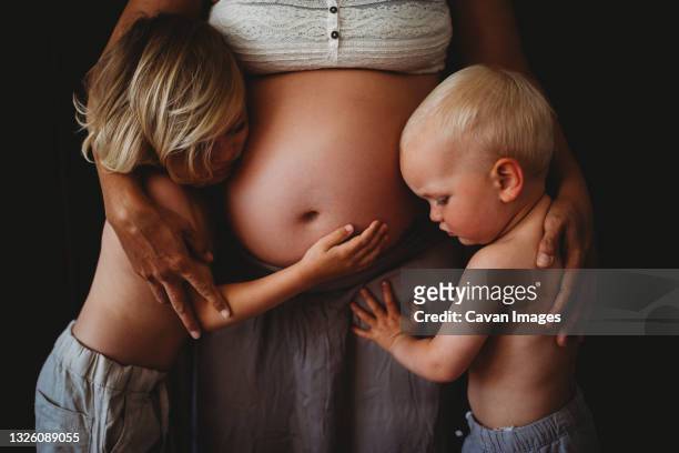 young blonde siblings hugging mom's pregnant big belly at home - baby touching belly fotografías e imágenes de stock