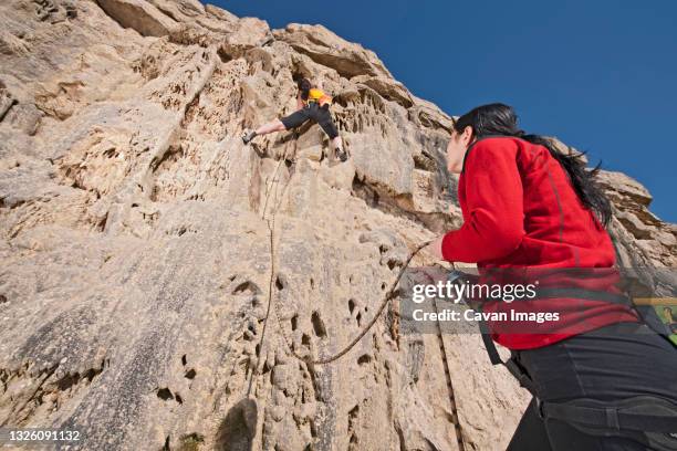 woman belaying for her friend at the limestone cliffs of swanage / uk - zekeren stockfoto's en -beelden