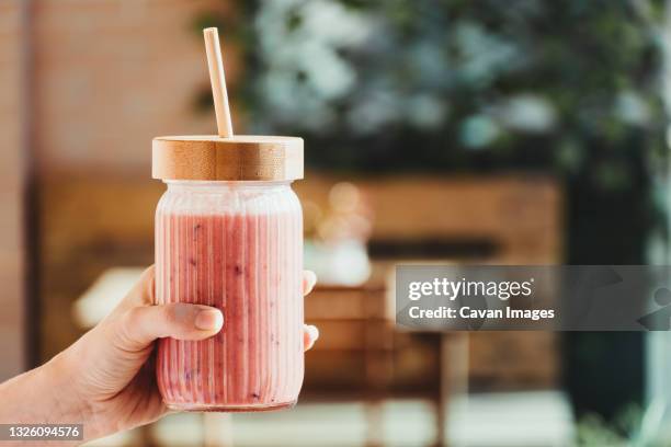 young woman's hand with a red fruit smoothie. - smoothies stockfoto's en -beelden