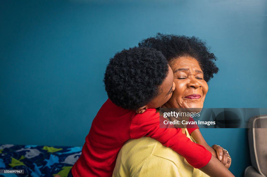 Grandson kissing grandmother on cheek by blue wall at home