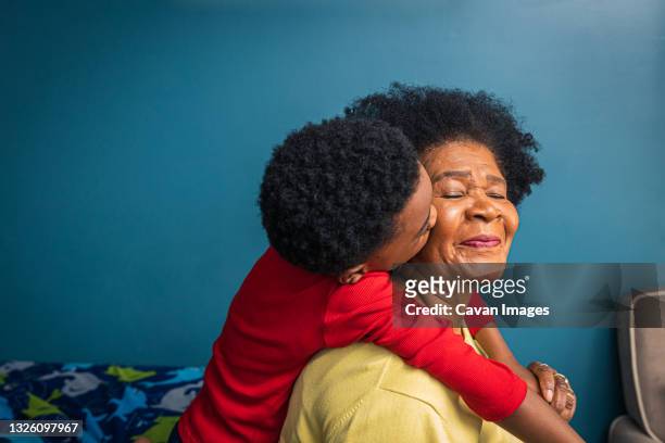 grandson kissing grandmother on cheek by blue wall at home - nieto fotografías e imágenes de stock