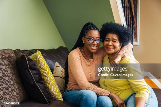 portrait of smiling senior woman with daughter sitting on sofa at home - generation gap stock pictures, royalty-free photos & images
