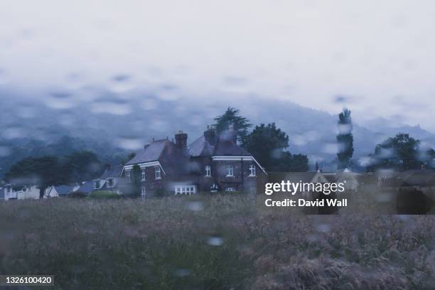 looking out onto an historic home across a field. as raindrops blur a car window. on a moody summers evening. uk - mystery car stock pictures, royalty-free photos & images