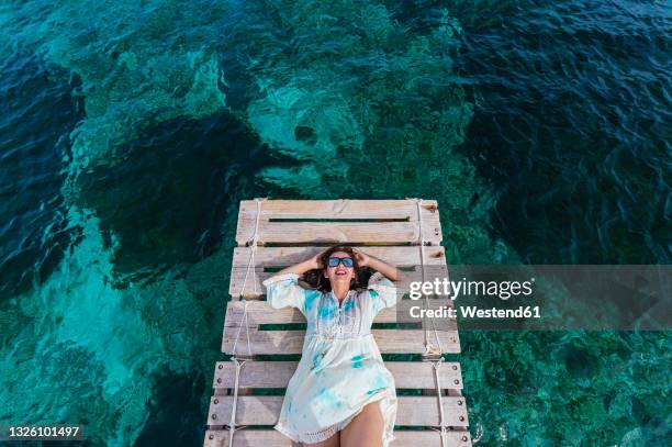 happy woman wearing sunglasses lying on jetty amidst water - islas baleares fotografías e imágenes de stock