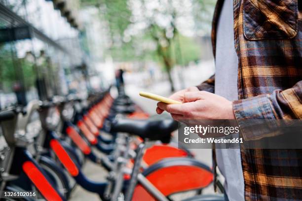 young man using smart phone at bicycle parking station - bicycle rental stock-fotos und bilder