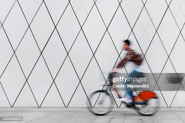 young man cycling on footpath by wall - bike sharing stock pictures, royalty-free photos & images