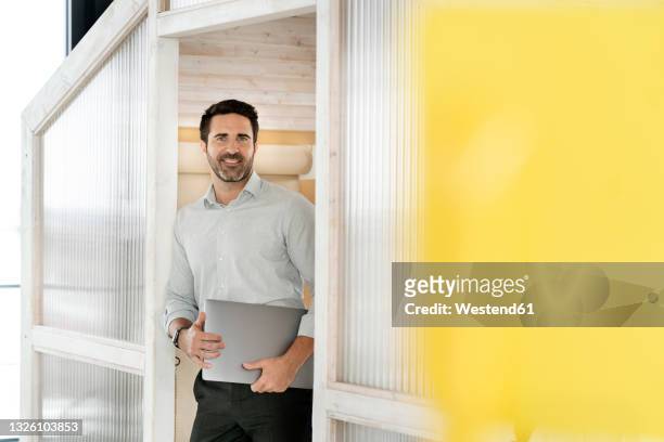 smiling male professional with laptop standing at cabin in office cafeteria - office cabin ストックフォトと画像