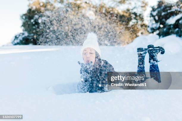 playful woman blowing snow while lying down - allongé sur le devant photos et images de collection
