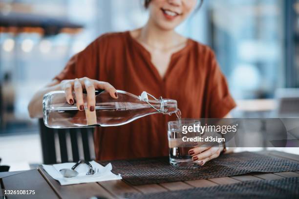 young asian woman pouring water from bottle into the glass at outdoor restaurant. healthy lifestyle and stay hydrated - 3 d glasses foto e immagini stock