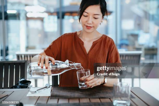 young asian woman pouring water from bottle into the glass at outdoor restaurant. healthy lifestyle and stay hydrated - 3 d glasses stock-fotos und bilder
