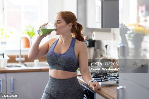 redhead woman drinking healthy milkshake after working out at home - smoothie and woman stockfoto's en -beelden