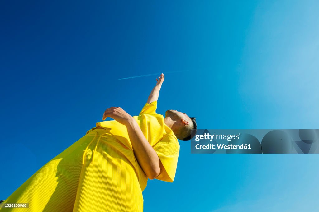 Young man looking up with hands raised in sky during sunny day
