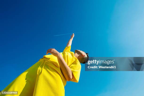 young man looking up with hands raised in sky during sunny day - olhar para cima imagens e fotografias de stock