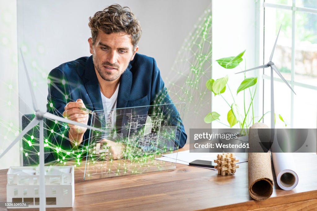 Male architect using futuristic digital tablet while sitting by desk