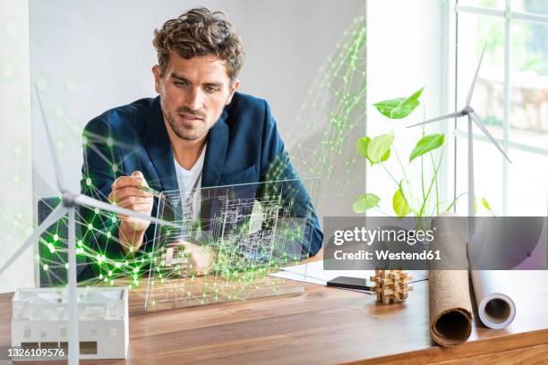 male architect using futuristic digital tablet while sitting by desk - green economy stockfoto's en -beelden