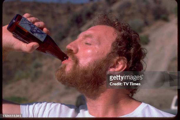 Actor Pat Roach in character as Brian 'Bomber' Busbridge drinking a bottle of beer on the Spanish set of comedy drama Auf Wiedersehen, Pet, circa...