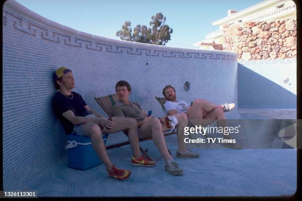 Actors Christopher Fairbank, Kevin Whately and Pat Roach sitting in an empty swimming pool on the set of comedy drama series Auf Wiedersehen, Pet,...