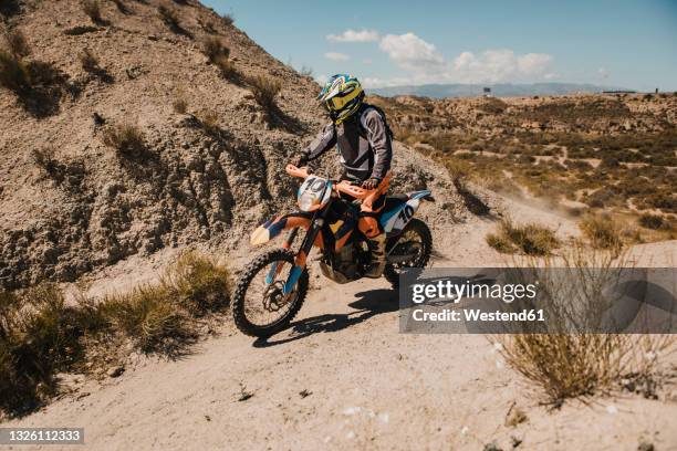 male biker in protective sportswear riding motorcycle on dirt road - scrambling fotografías e imágenes de stock