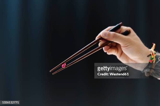 man holding capsule with chopsticks against black background - eetstokje stockfoto's en -beelden