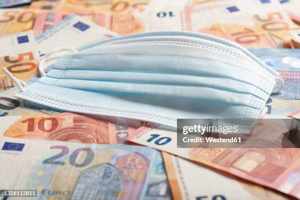 protective face mask lying on top of pile of money symbolizing making business thanks to covid-19 pandemic - corruption imagens e fotografias de stock