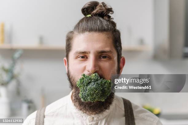 mid adult man staring with broccoli in mouth at home - funny vegetable stock-fotos und bilder