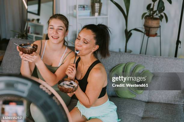 female fitness trainers eating fruit bowls while vlogging at home - calcio sport imagens e fotografias de stock