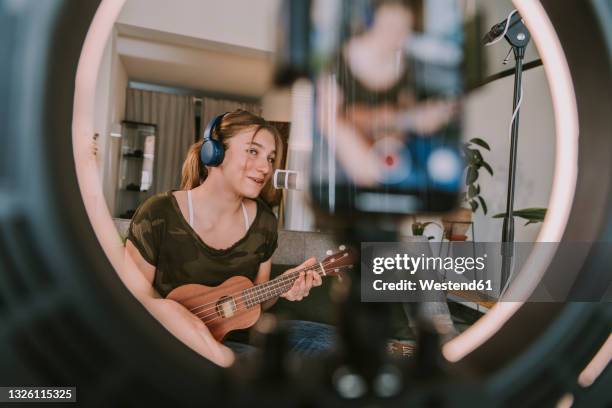 girl singing on microphone while playing ukulele at home - darstellender künstler stock-fotos und bilder