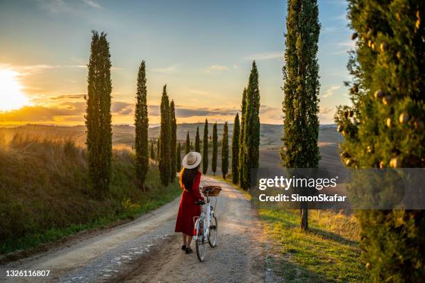 夕暮れ時にヴィンテージ自転車を持つ若い女の子 - red dress ストックフォトと画像