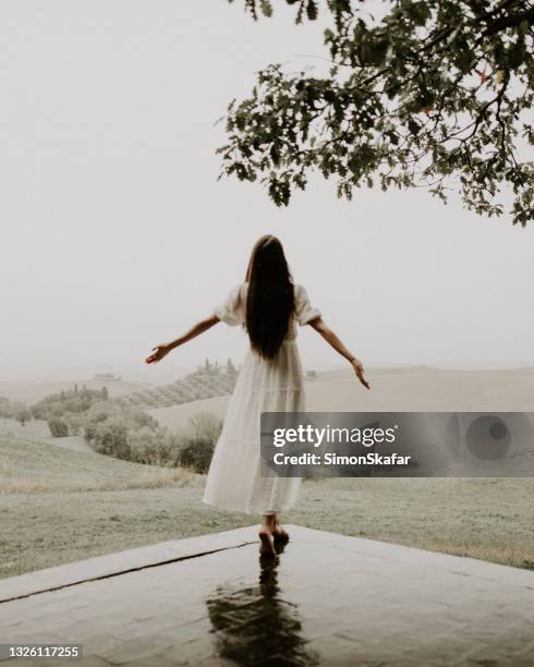 vue arrière d’une jeune femme profitant sous la pluie - les bras écartés photos et images de collection