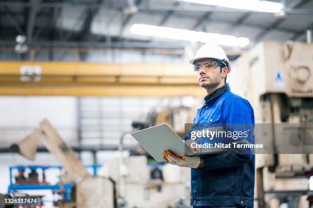auto part production in the automobile industry. portrait of a production line surveyor engineer working at a large hydraulic stamping press machine and holding a laptop. he expert in planning, improvement, and monitoring of the production processes. - factory workers stockfoto's en -beelden