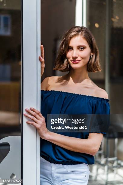 smiling female entrepreneur with medium length hair standing at doorway - alleen één jonge vrouw stockfoto's en -beelden