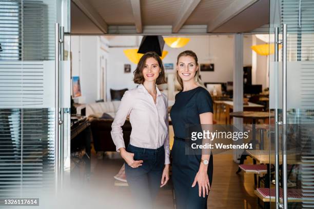 smiling female professionals standing together at doorway in office - two people portrait stock pictures, royalty-free photos & images