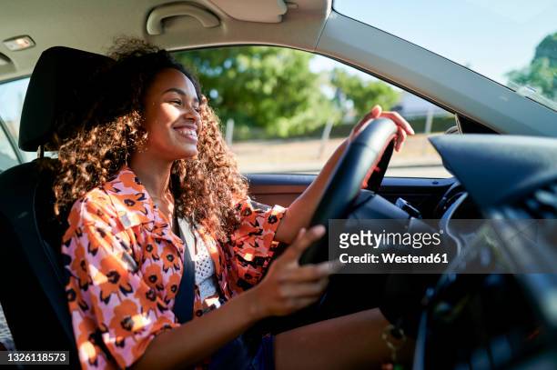 smiling young woman driving car - car drive stock-fotos und bilder