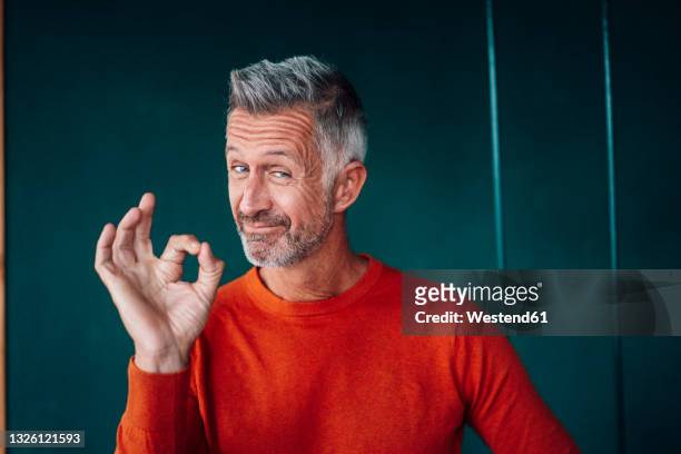 mature man gesturing ok sign in front of wall - esprimere a gesti foto e immagini stock