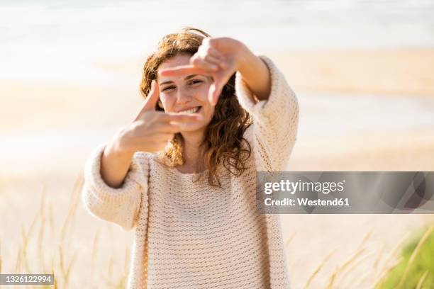 happy woman looking through finger frame at beach during sunny day - dedos fazendo moldura - fotografias e filmes do acervo