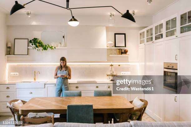 pregnant woman using smart phone in domestic kitchen - pendant light - fotografias e filmes do acervo