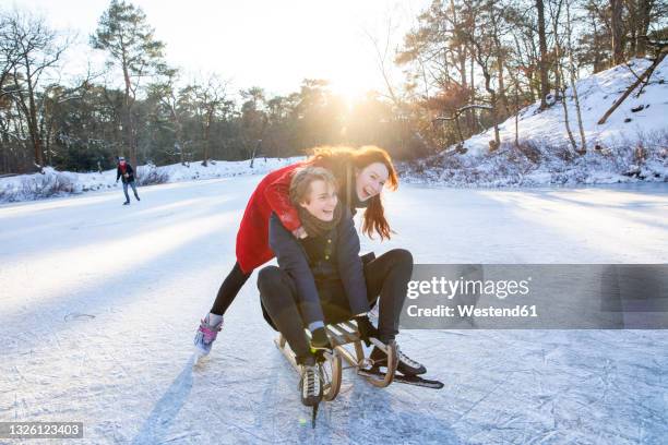 cheerful couple enjoying sledding and ice-skating on frozen lake - outdoor skating stock pictures, royalty-free photos & images