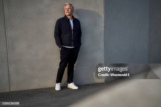 mature male professional standing with hands in pockets in front of wall - 50 sombras fotografías e imágenes de stock