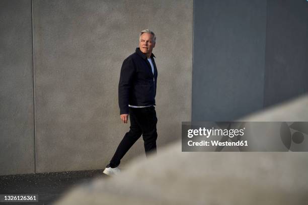 mature businessman looking over shoulder while walking by wall - over shoulder stock-fotos und bilder