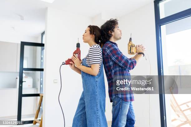 playful couple holding drill machines while relocating in new home - mid adult women stock pictures, royalty-free photos & images