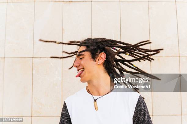 man with dreadlocks shaking head while sticking out tongue in front of wall - haare schütteln stock-fotos und bilder