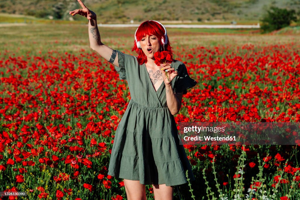 Young woman holding bunch of flowers while singing on poppy field