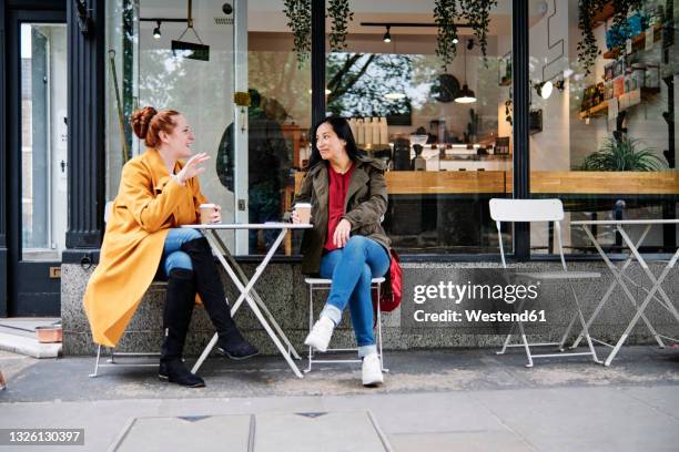 woman gesturing while talking with female friend outside coffee shop - women friends stock pictures, royalty-free photos & images